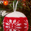 A knitted Christmas bauble in red and white, with a bold, geometric pattern, hanging on a Christmas tree.