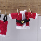 Knitted Santa Claus outfit hanging on a line with wooden pegs against a wooden background.