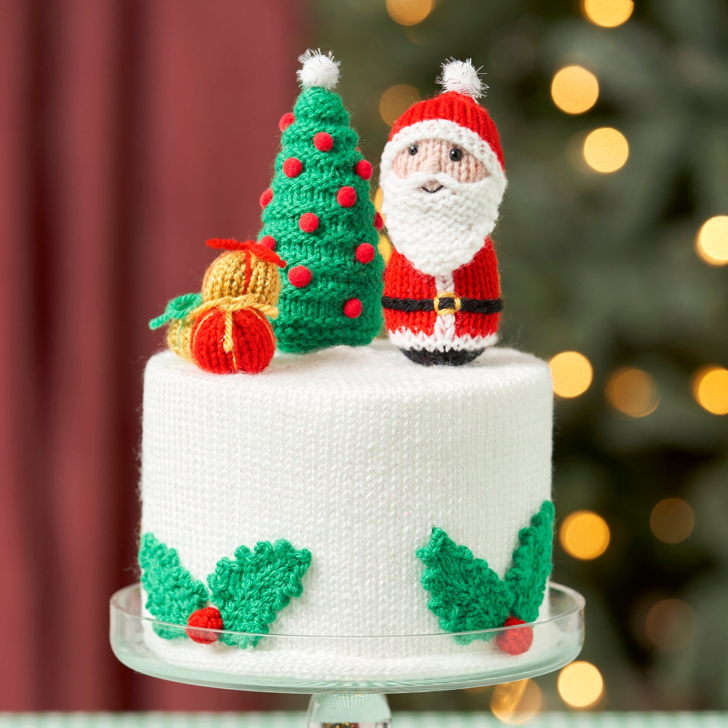 Knitted Christmas cake topper with Santa Claus and tree on a blurred festive background