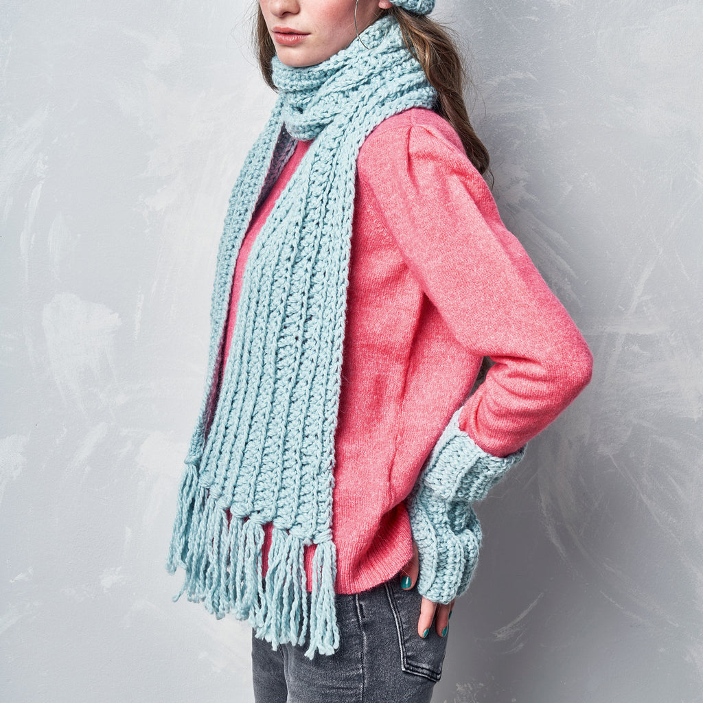 Person wearing a pink sweater, light blue scarf, and matching gloves against a gray background