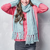 Person wearing a long light blue scarf with tassels on a plain background