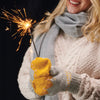 A person wearing a grey and yellow colour block knitting pattern mitten holding a sparkler.