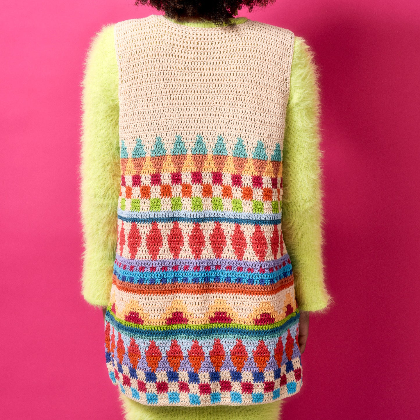 Person wearing a colorful crochet vest against a pink background