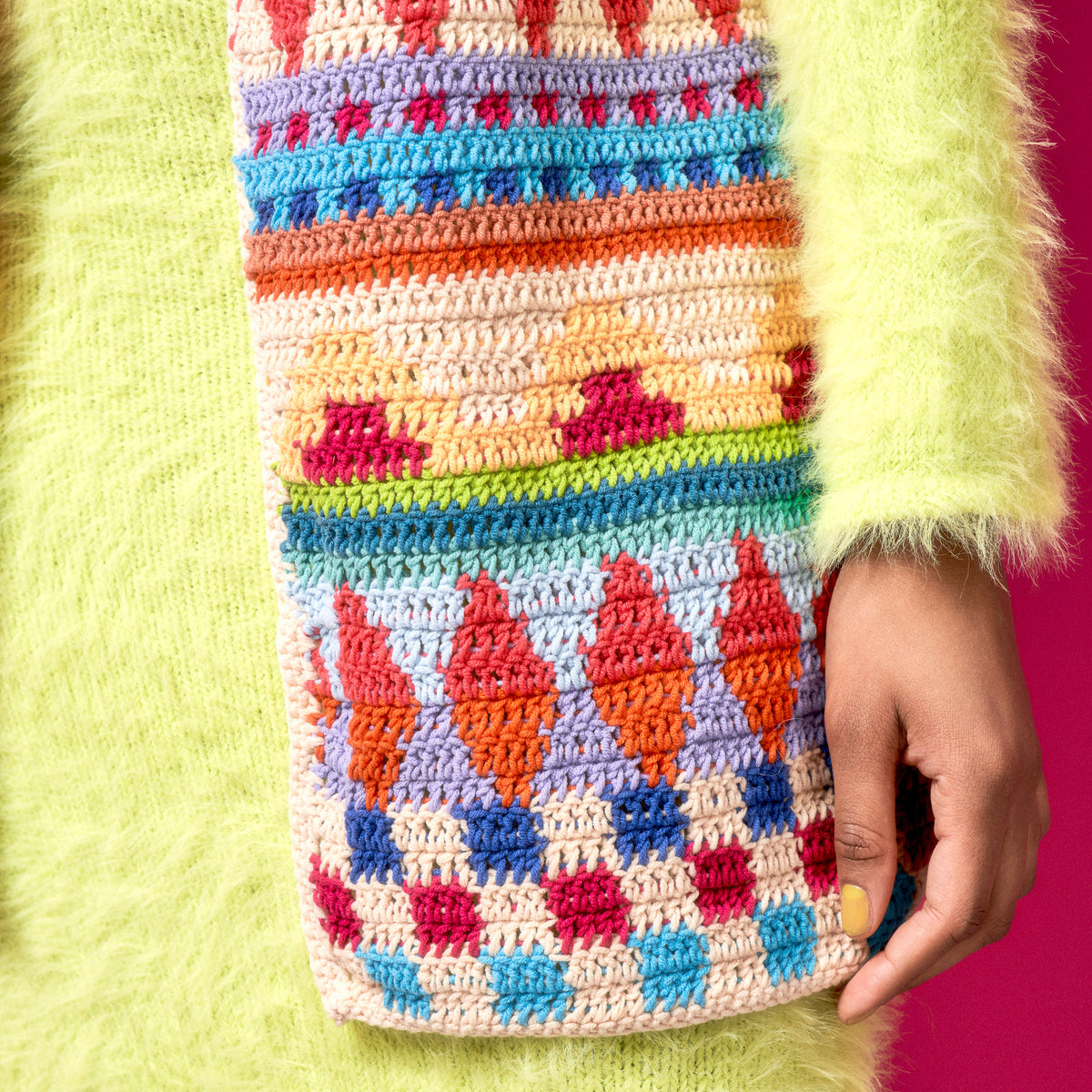 Colorful crocheted patterned pouch held by a person wearing a green sweater.