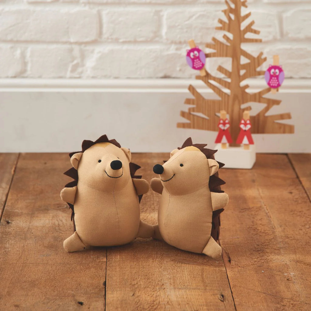Two plush hedgehogs on a wooden floor with a decorative Christmas tree in the background.