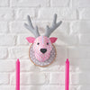 Decorative deer head with pink and gray antlers on a white brick wall.
