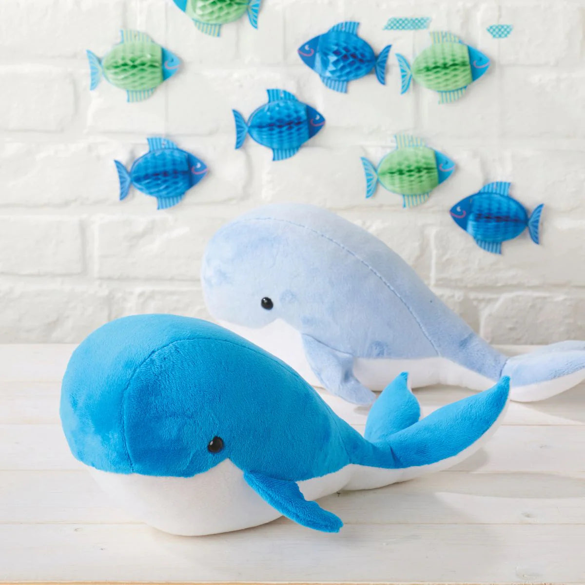 Two blue plush whales with small fish toys on a textured white background