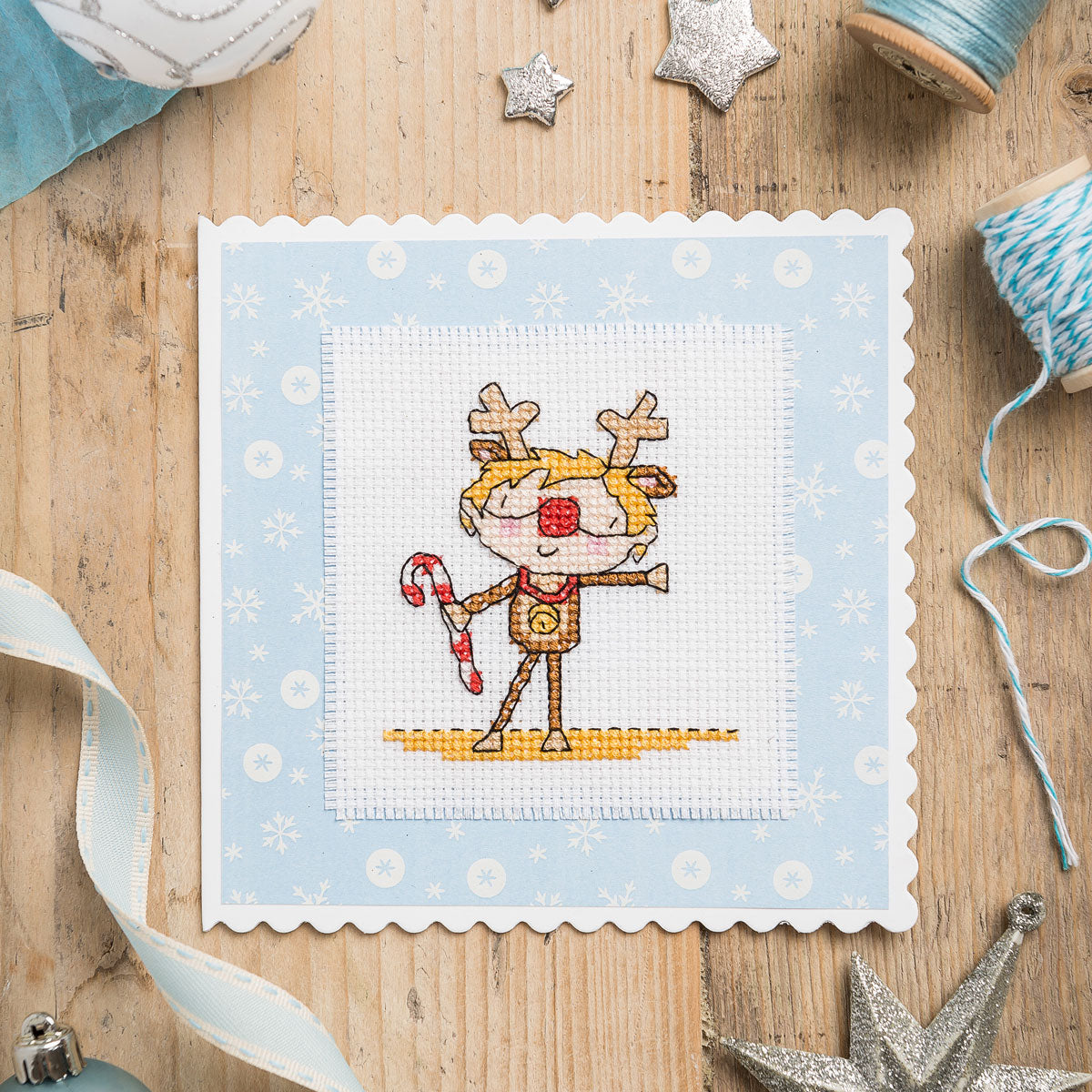 Cross-stitched reindeer design on a blue fabric background with Christmas decorations around.