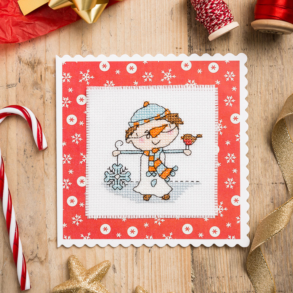 Cross-stitched design of a winter scene with snowflakes on a wooden surface with Christmas decorations.