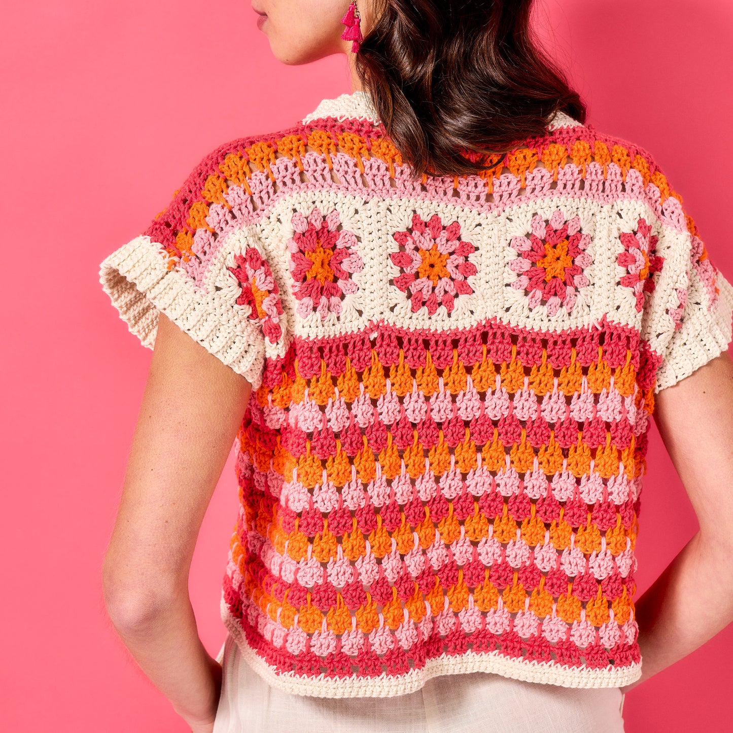 Person wearing a colorful crochet patterned shirt against a pink background