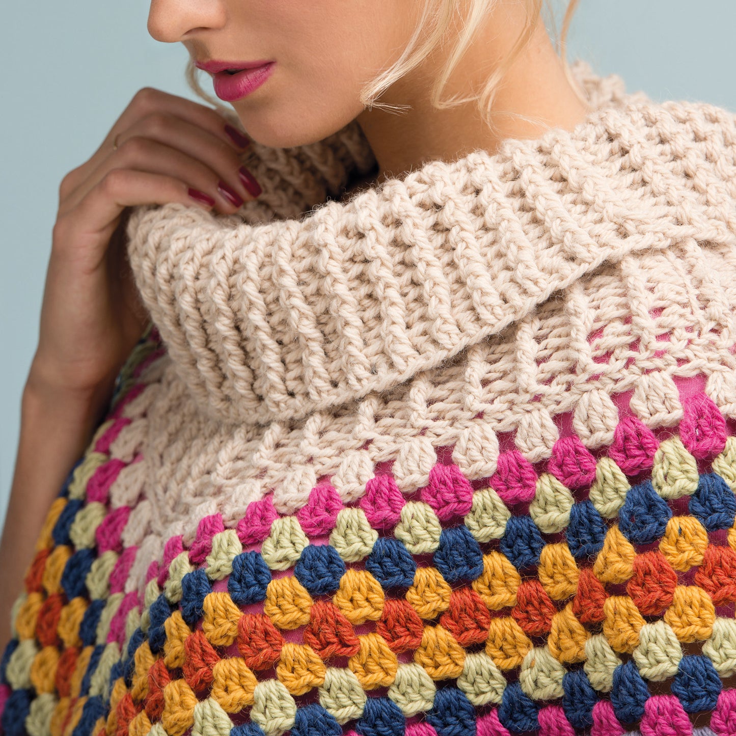Close-up of a woman's face and shoulder, showcasing a colorful crochet sweater with a chunky, beige turtleneck. The mood is cozy and stylish.