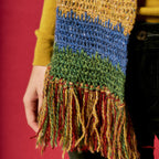 Colorful knitted scarf with fringe held by a person against a red background