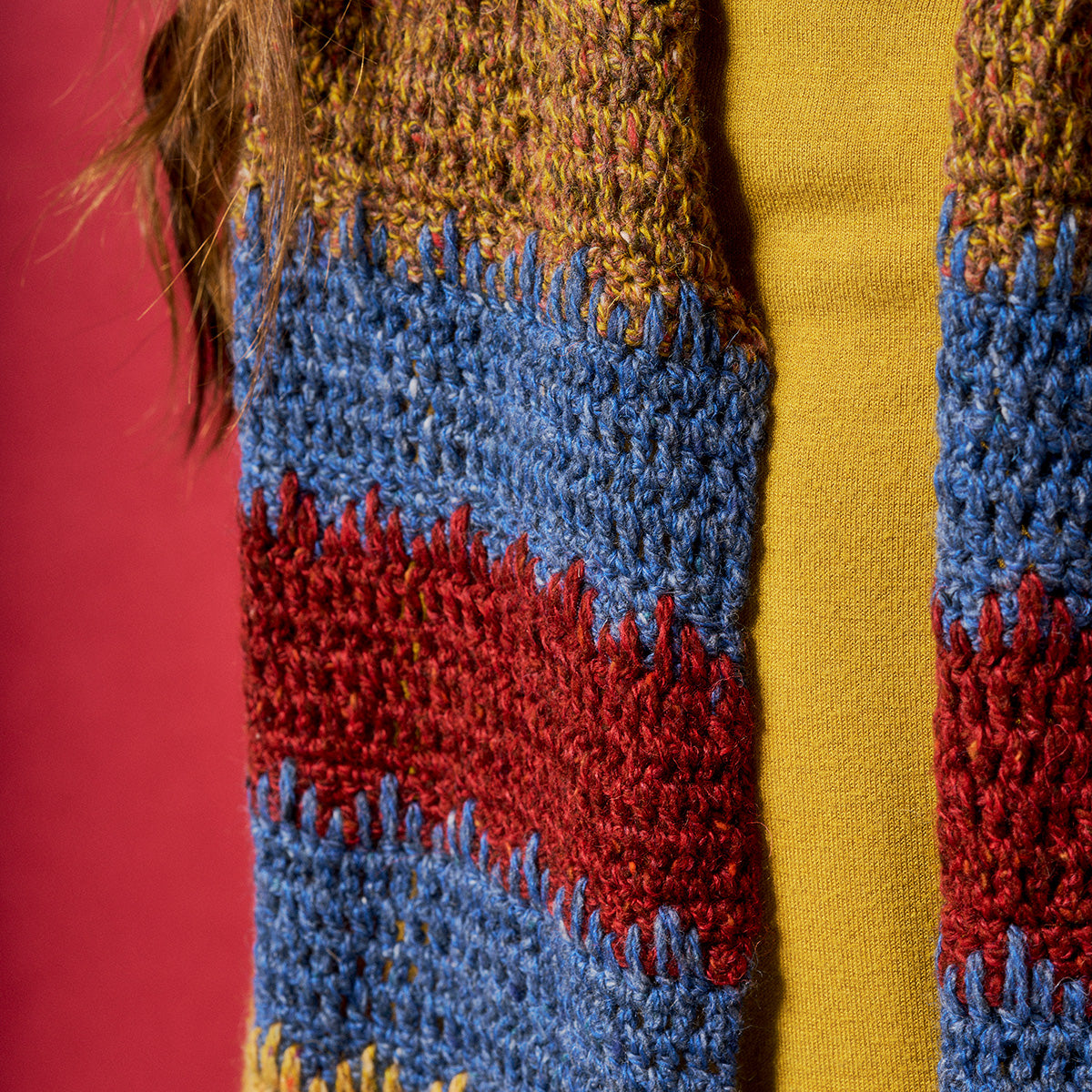 Close-up of a colorful crochet scarf with blue, red, and yellow patterns on a red background.
