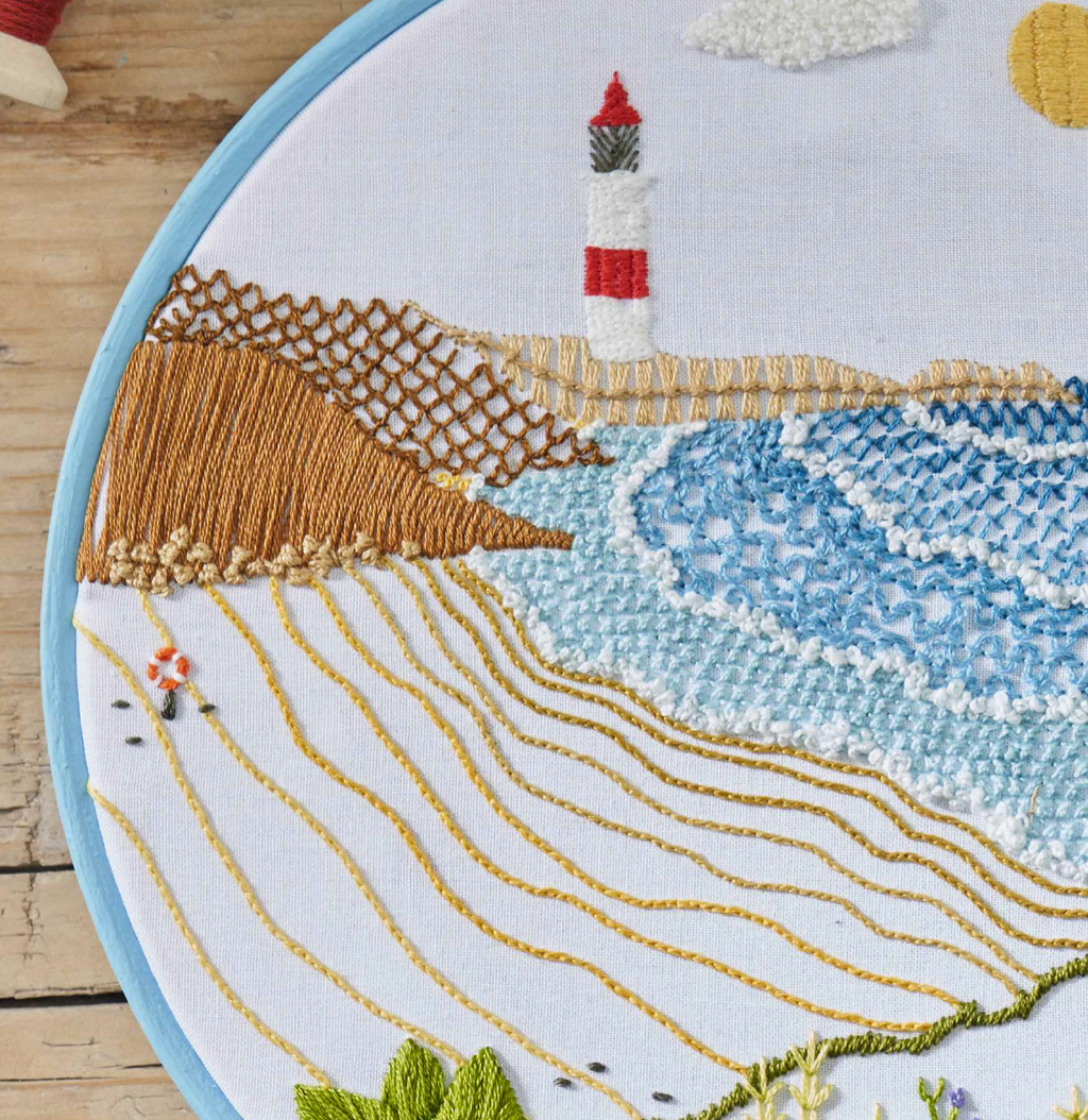 Embroidery hoop with a scenic design featuring a lighthouse, beach, and sea.