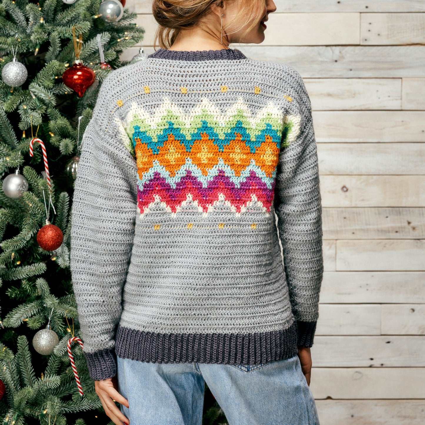 Person wearing a colorful patterned sweater standing next to a decorated Christmas tree.