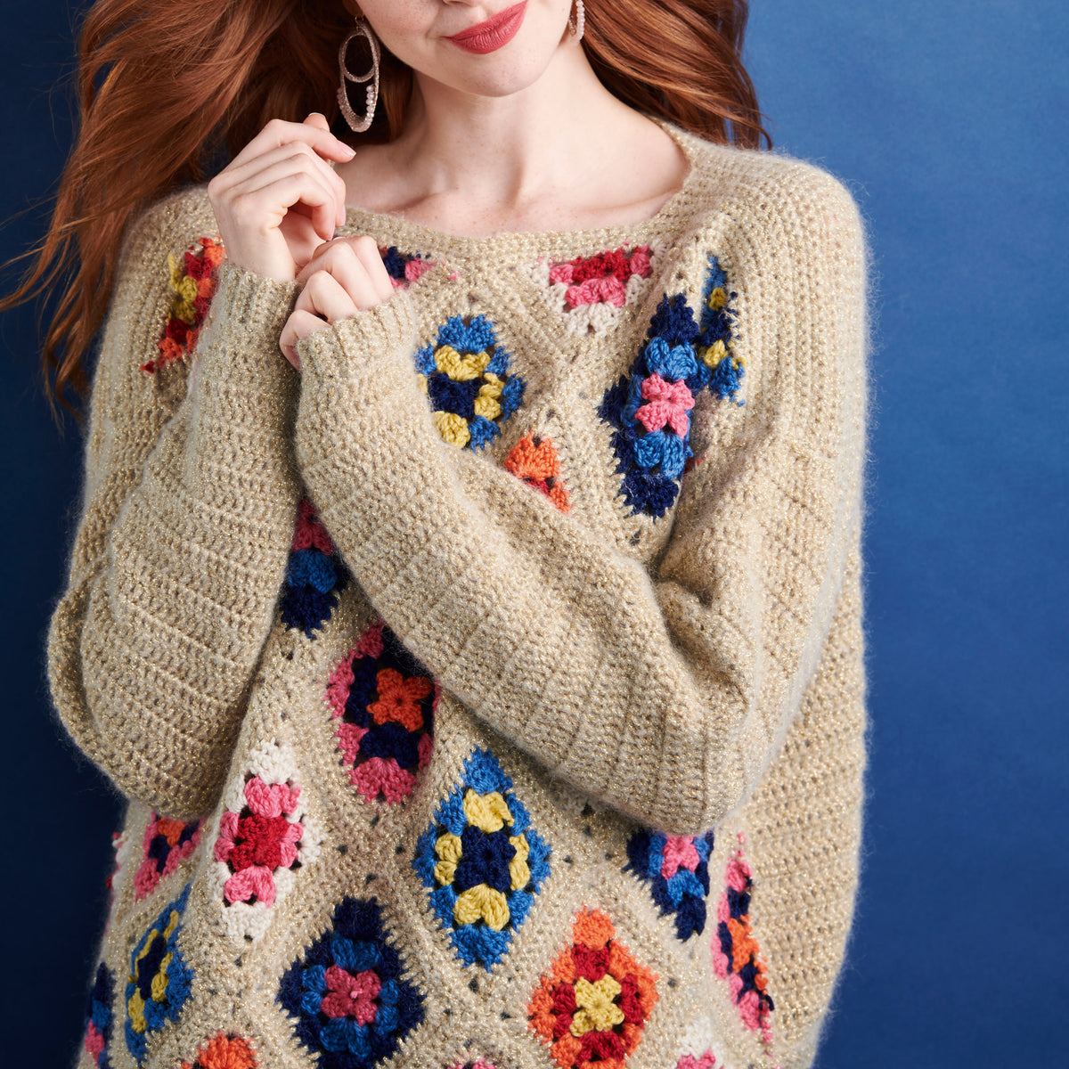 Beige sweater with colorful floral patterns worn by a person against a blue background