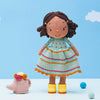 A crochet pattern of a girl doll with a striped dress and a garden-themed outfit, accompanied by a small crochet chicken and decorative balls.