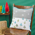 Crocheted pillow with Christmas tree pattern on a wooden chair against a green background