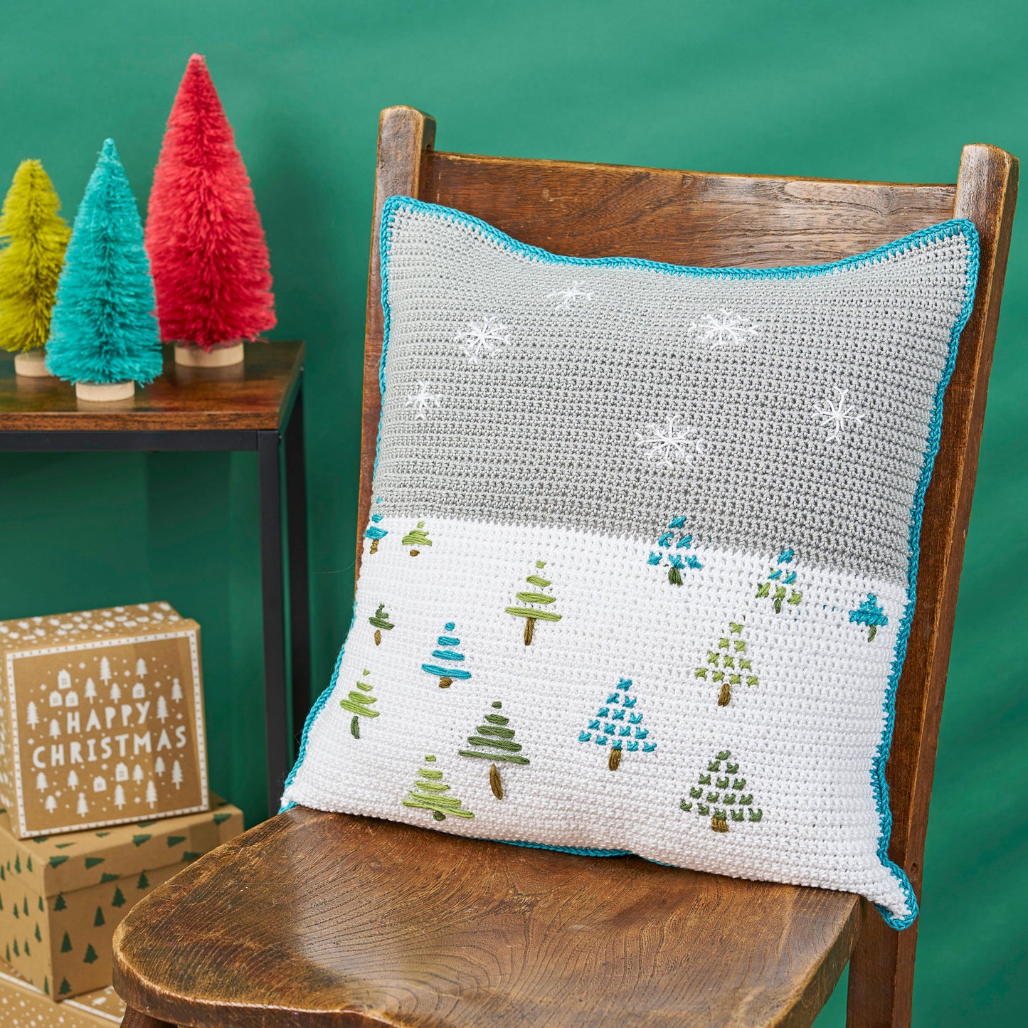 Crocheted pillow with Christmas tree pattern on a wooden chair against a green background