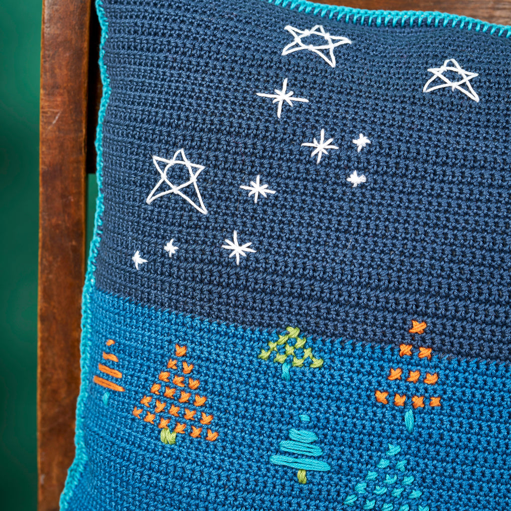 Blue crocheted blanket with embroidered stars and trees on a wooden surface.