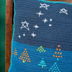 Blue crocheted blanket with embroidered stars and trees on a wooden surface.