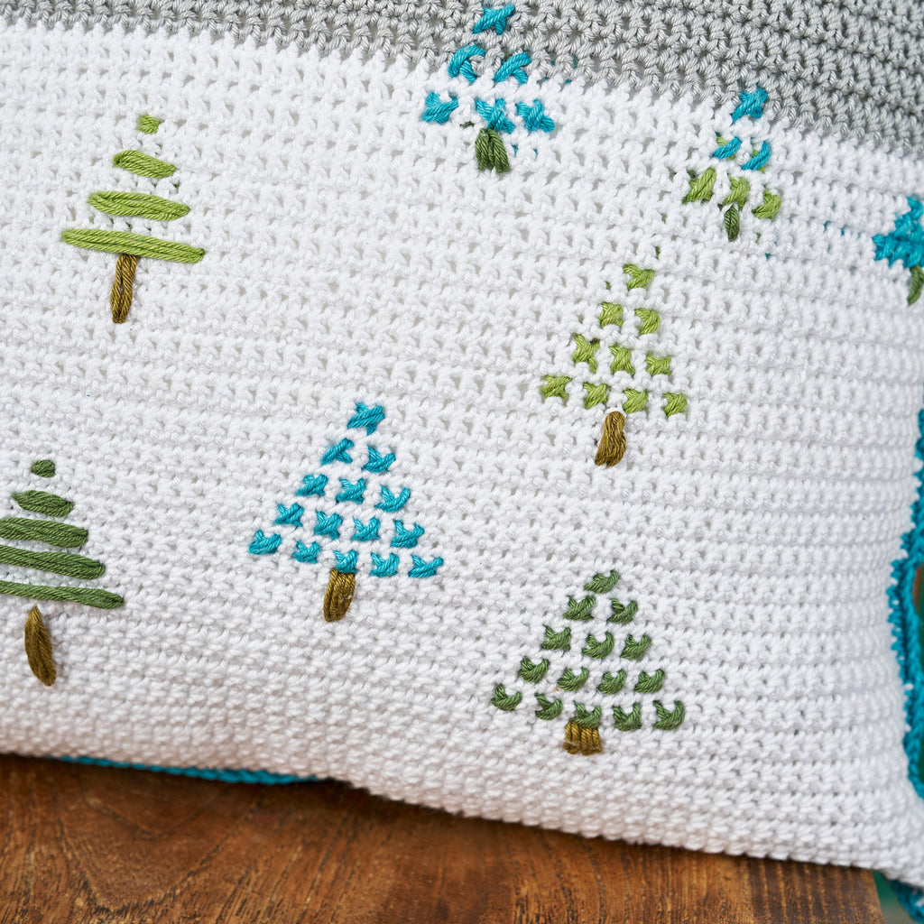Cross-stitched pattern of trees on a white fabric background