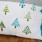 Cross-stitched pattern of trees on a white fabric background