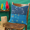 Crocheted pillow with Christmas tree design on a wooden chair against a green background.
