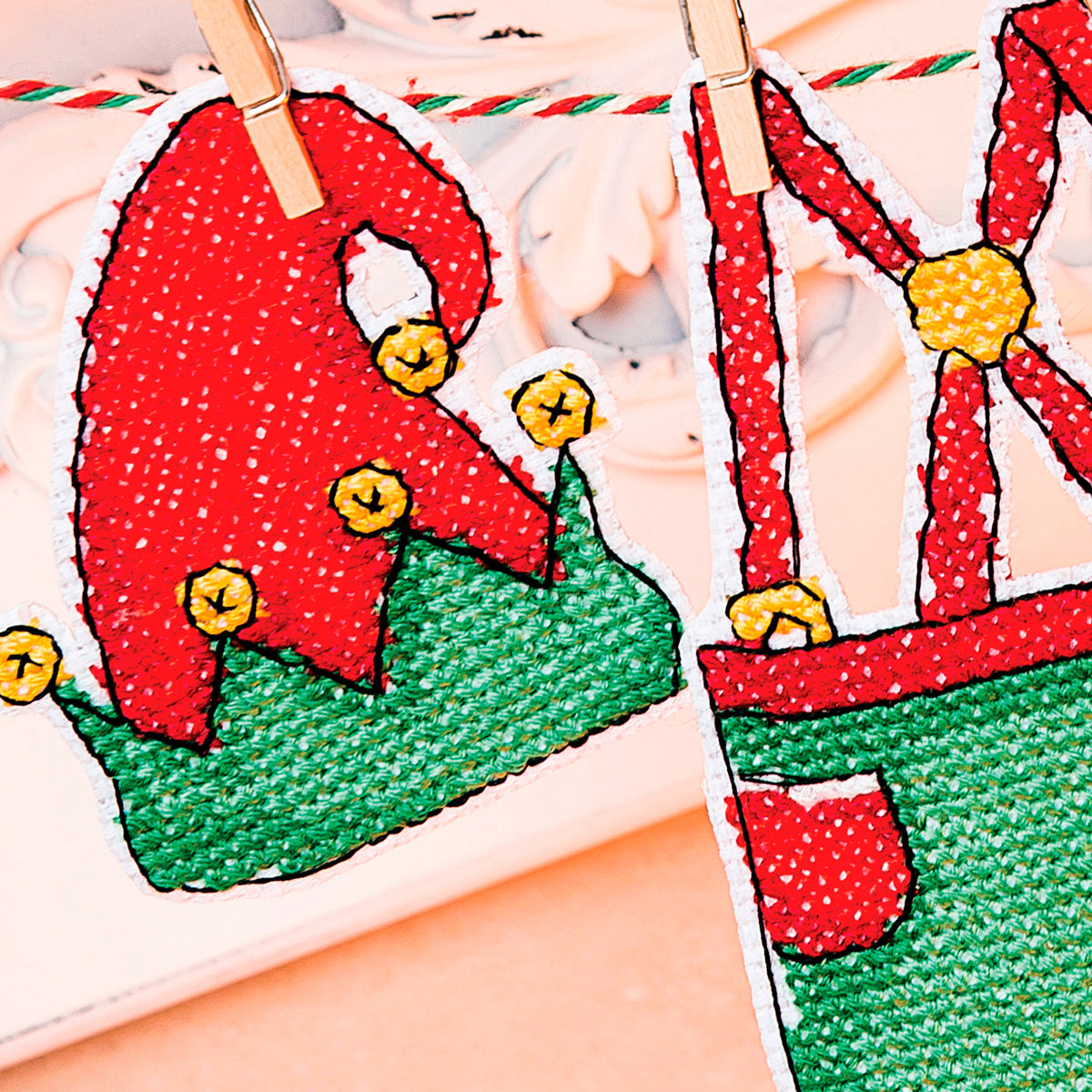 Two cross stitch patches of a red elf hat and green pants on a white background.