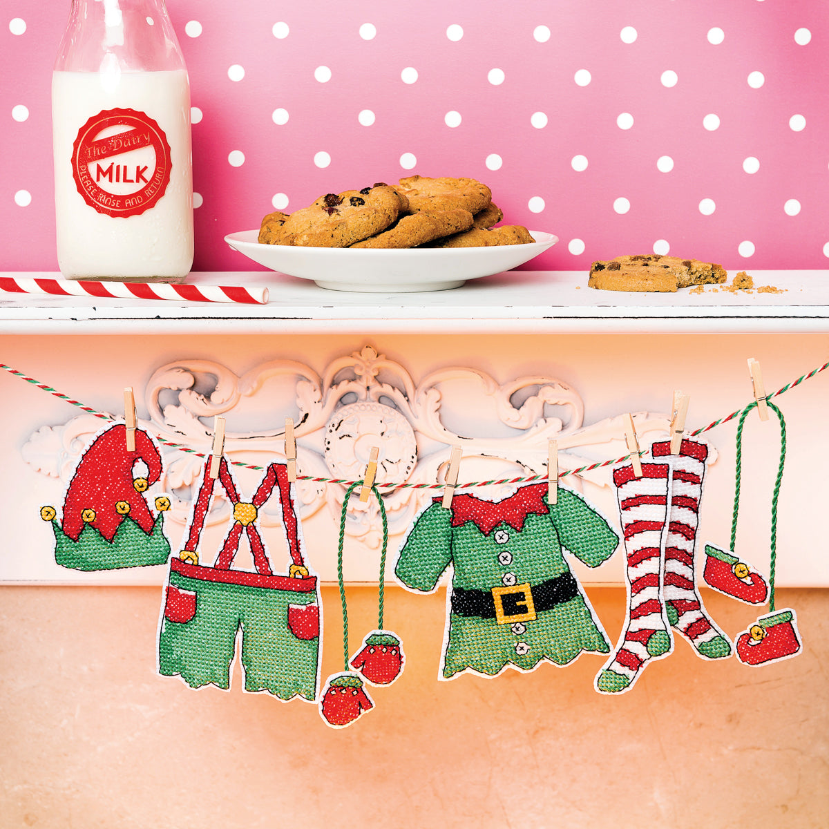 Decorative Christmas-themed clothesline with elf outfits on a pink polka dot wall.