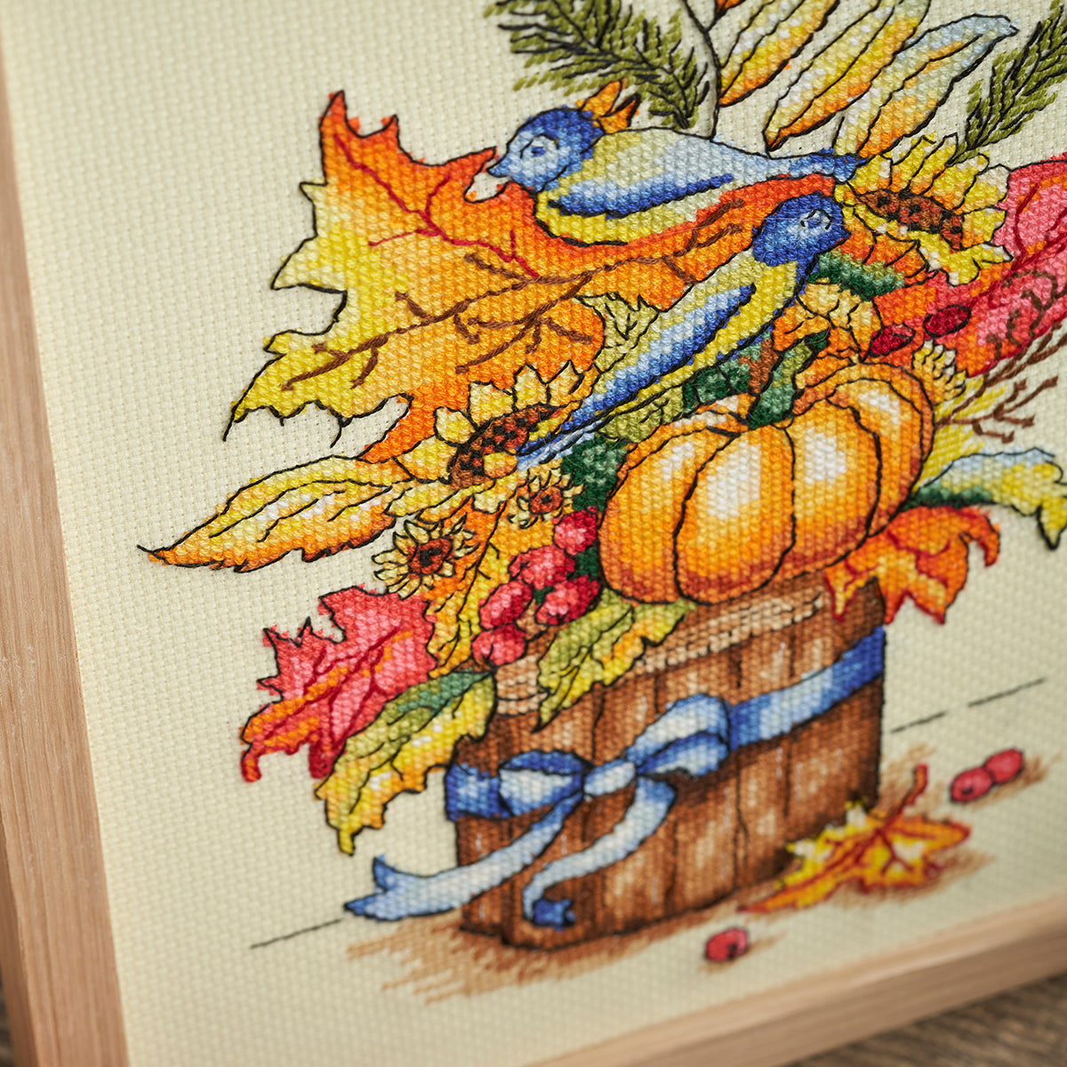 Cross-stitched piece depicting autumn elements with leaves, pumpkins, and a bird.