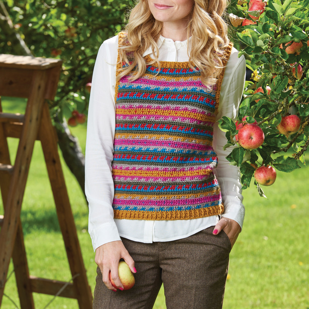 Woman wearing a colorful striped apron outdoors with greenery and apples in the background