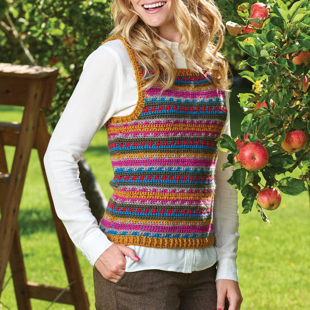 Woman wearing a colorful striped vest outdoors with greenery and apples in the background