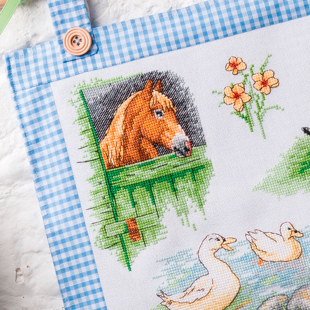 Cross-stitched design with a horse and ducks on a checkered fabric background