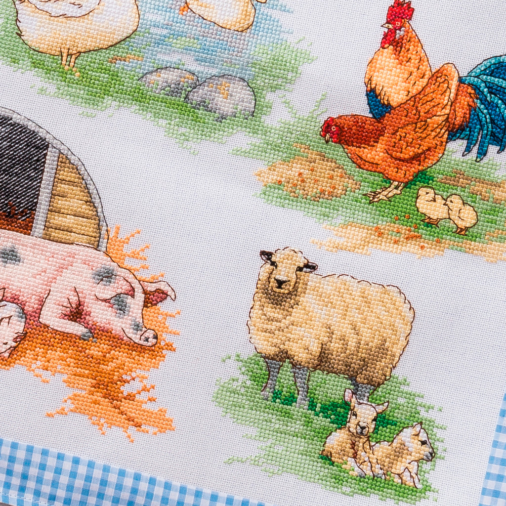 Cross-stitched pattern of farm animals including a rooster, sheep, and pig on fabric.