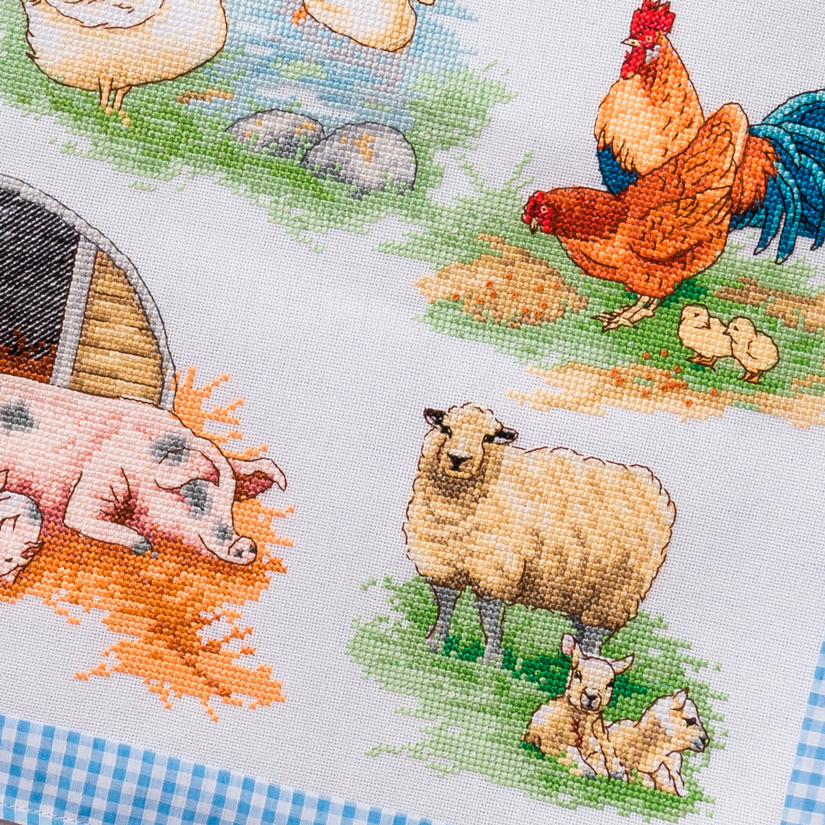 Cross-stitched pattern of farm animals including a rooster, sheep, and pig on fabric.