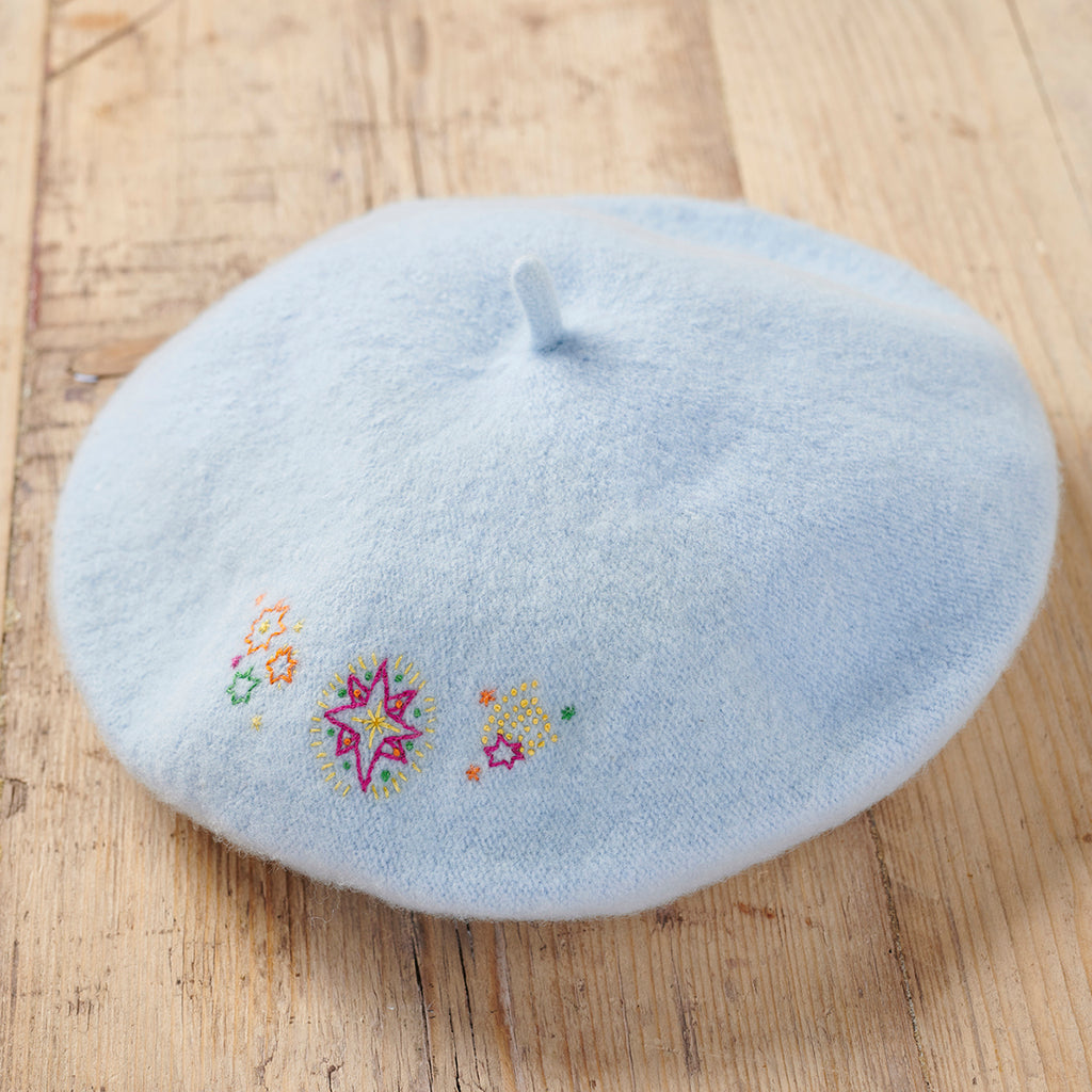 Light blue beret with embroidered designs on a wooden surface