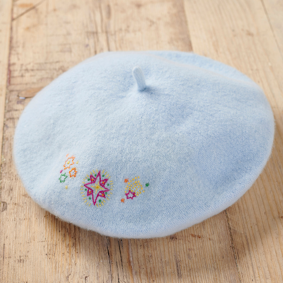 Light blue beret with embroidered designs on a wooden surface