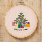 Embroidery hoop with a Christmas tree and presents design on a wooden surface