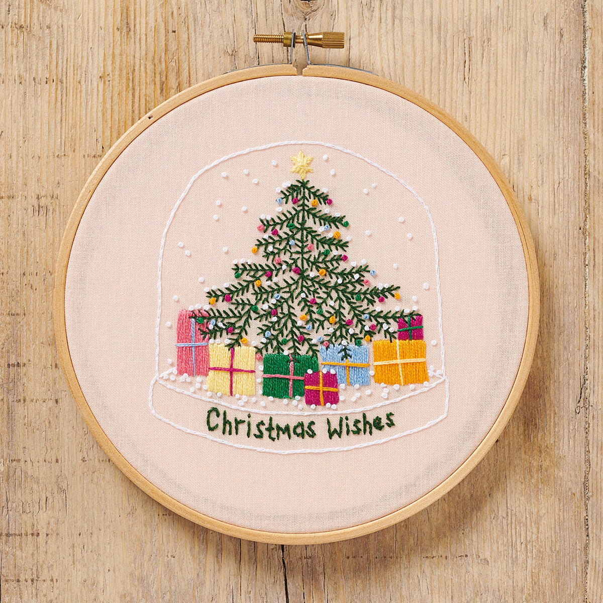 Embroidery hoop with a Christmas tree and presents design on a wooden surface