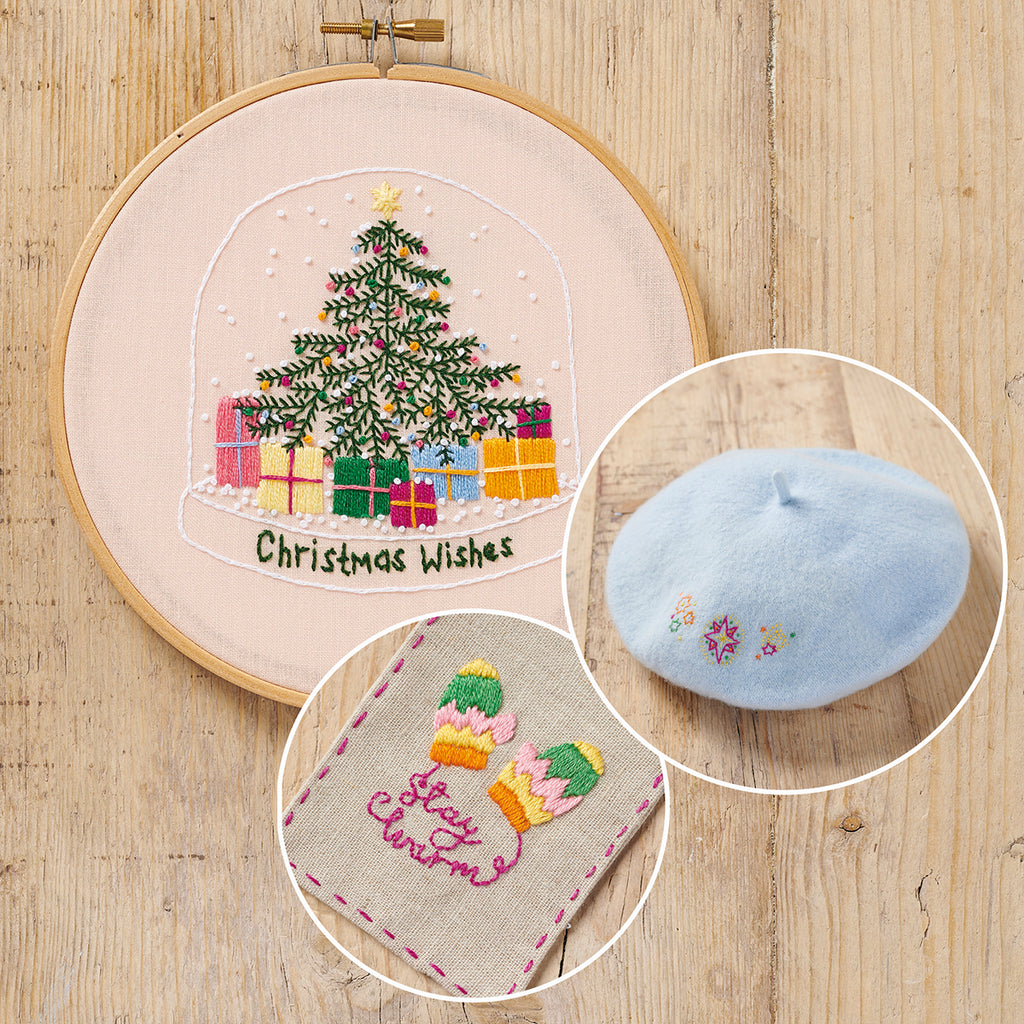 Embroidery hoop with Christmas-themed embroidery, small blue beret, and fabric patch on a wooden surface.