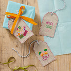Embroidered gift tags with colorful designs and text on a wooden surface
