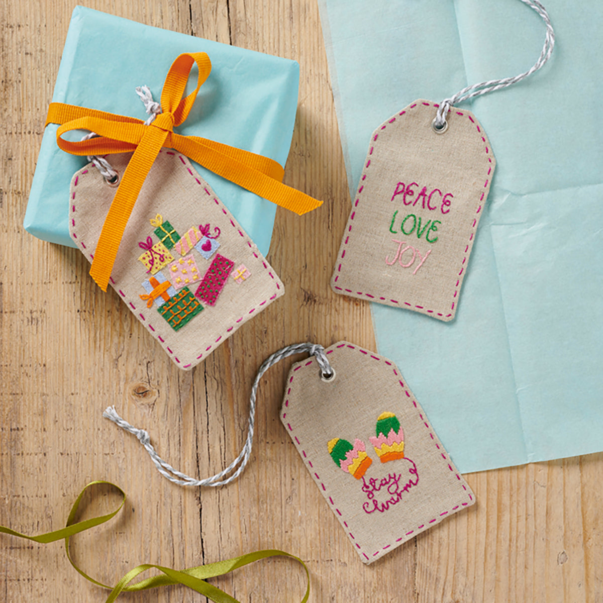 Embroidered gift tags with colorful designs and text on a wooden surface