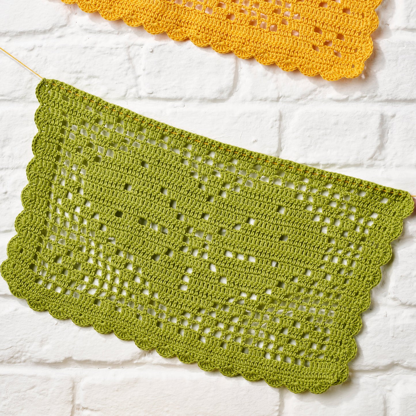 Green crocheted doily on a white brick wall background