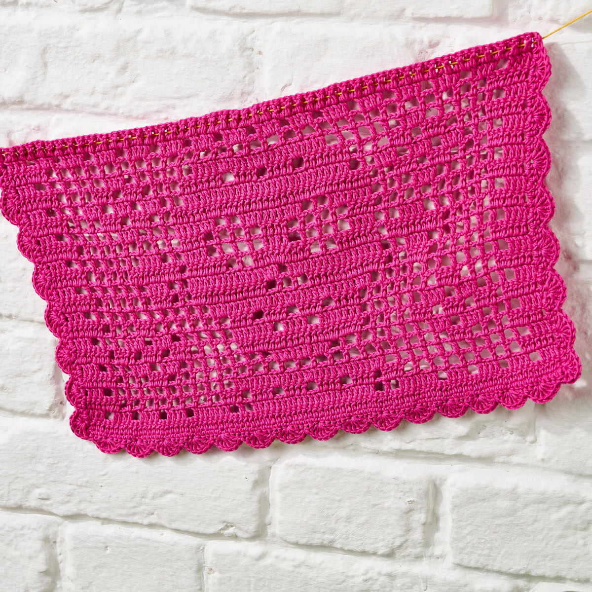 Pink crocheted fabric on a white brick wall background