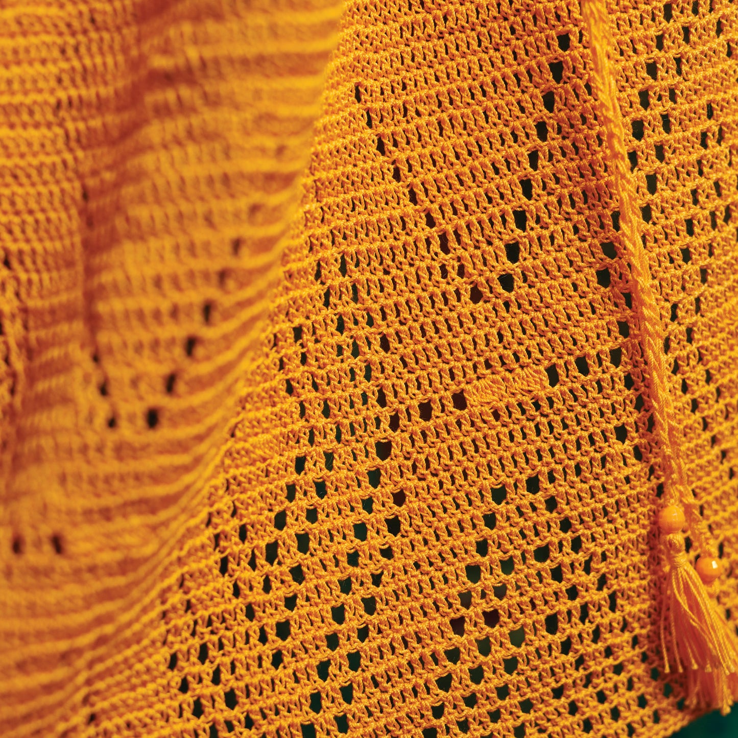 Close-up of a vibrant orange crochet fabric with intricate patterns and a tassel, conveying a warm and textured aesthetic.