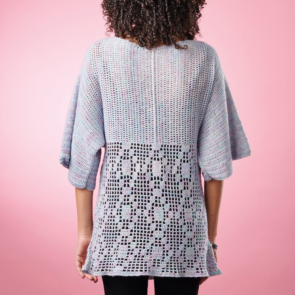 Person wearing a light blue crochet cardigan against a pink background
