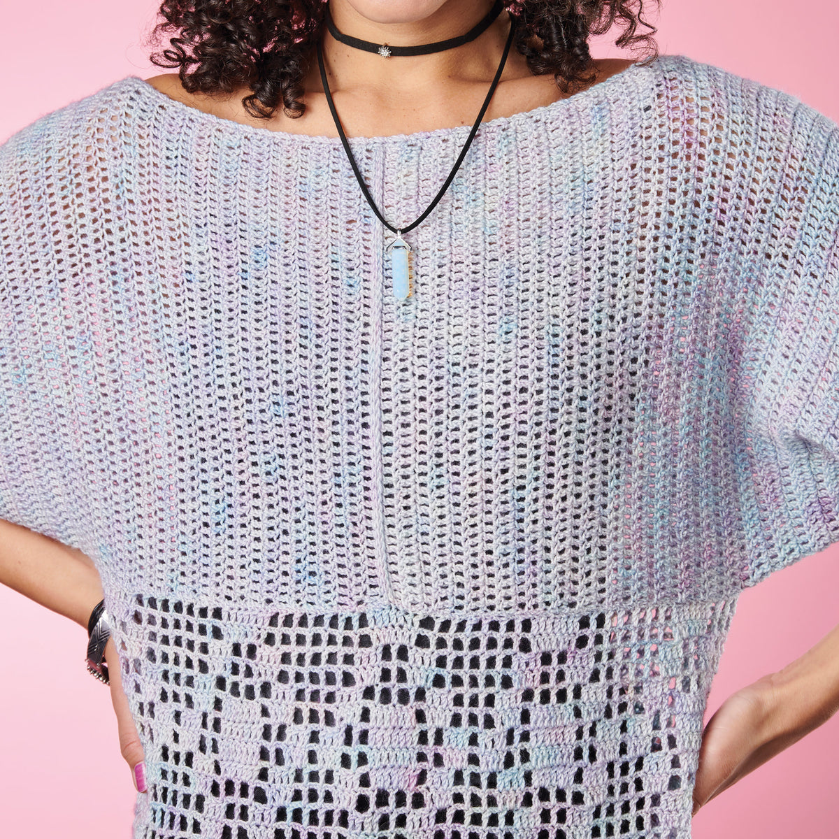 Person wearing a light blue crochet top against a pink background