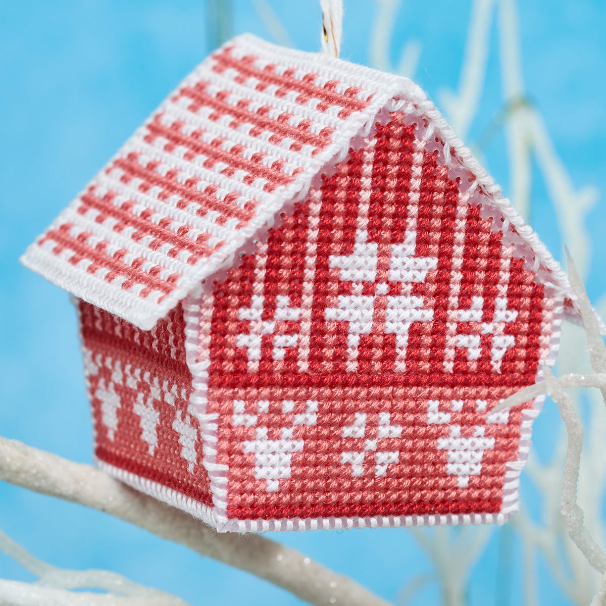 Decorative red and white house ornament with reindeer pattern on a branch against a blue background