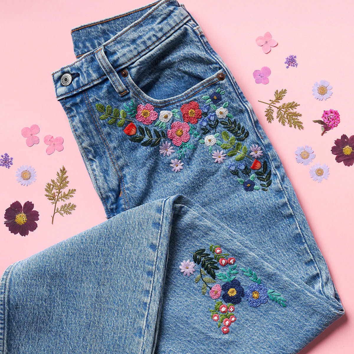 Embroidered jeans with floral designs on a pink background